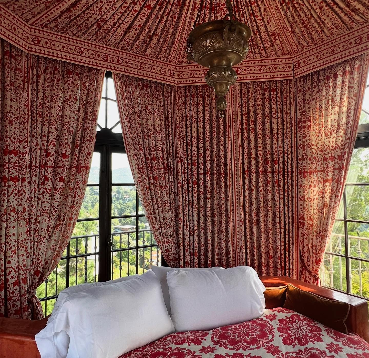 A richly patterned red bedroom with windows overlooking the hills